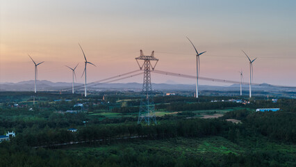 Wind turbines and power transmission towers at sunset in rural area