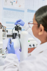 Researcher feeds plastic filament into an injection-based 3D printer during a laboratory setup process, wearing appropriate lab attire.