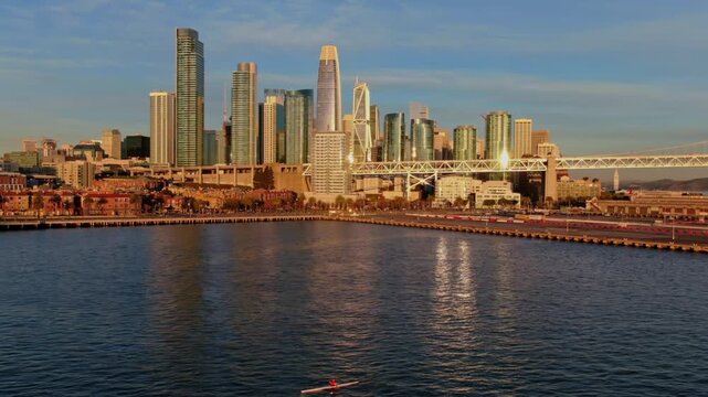 A lone rower practices on the bay in San Francisco, USA, with the city skyline and bridge in the background. The rower is training for a competition.