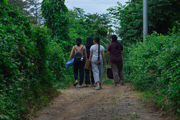 The girls move slowly under the forest canopy, glancing around as they walk and absorb the natural...