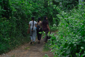 Walking side by side, the girls take time to look around and enjoy the lush forest surroundings as...