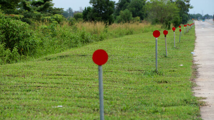 A row of red circular reflectors on metal poles lines the grassy roadside of a quiet highway, providing safety markers for drivers                         