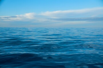 Obraz premium Calm Blue Ocean Waters Under a Sky Partially Covered by Soft White Clouds on a Clear Day in Summertime