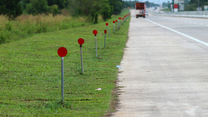 A row of red circular reflectors on metal poles lines the grassy roadside of a quiet highway, providing safety markers for drivers                         