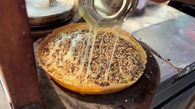 A sweet martabak (terang bulan), generously topped with chocolate sprinkles and rich condensed milk drizzles, is captured in this close-up, showcasing the final