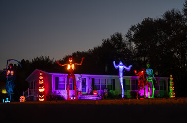 Halloween night house exterior with spooky decor. Scary skeleton in front yard. Home decorated with...