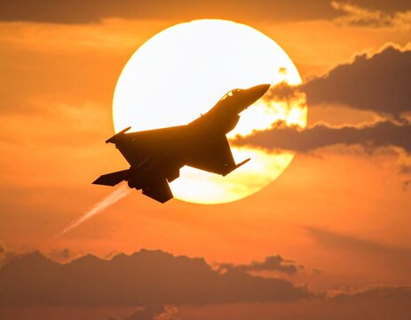 Silhouette of a fighter jet flying against a vibrant sunset, leaving a contrail in the orange sky with scattered clouds. - Powered by Adobe