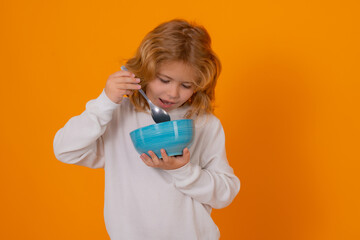 Child eating breakfast with spoon and bowl. Funny boy enjoying tasty dairy product. Kid holding cup...
