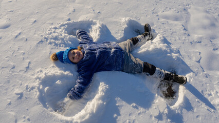 Kid and snow in the park. Kid plays joyfully in snowfall. Winter kids portrait. Snowflakes on happy...