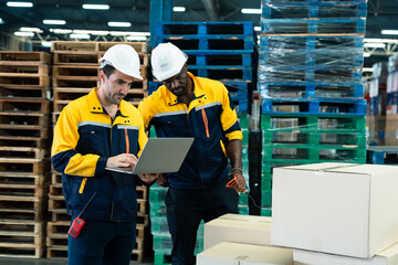 Two male warehouse workers analyzing delivery data together using laptop and scanner inside...