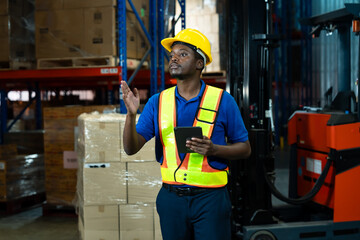 Black adult male warehouse worker raising hand and holding tablet while communicating inside...