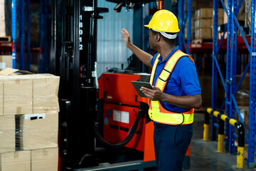 African male adult warehouse worker pointing at goods while holding tablet standing in logistics...