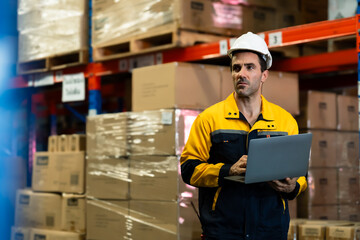 male adult caucasian supervisor in warehouse inspecting goods using laptop computer while standing...