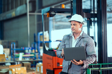 Caucasian male foreman in gray uniform and white hardhat standing confidently with laptop near...