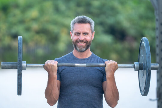 40s man doing fitness exercises. Healthy workout. Miami beach fitness model with barbell. Healthy lifestyle barbell training. Mature man exercising with barbell outdoors. Man lifting barbell.