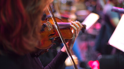 girl playing violin in orchestra on stage,