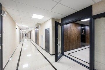 Long, modern hallway with white tiled floor, dark doors, and a glass door leading to suite 5