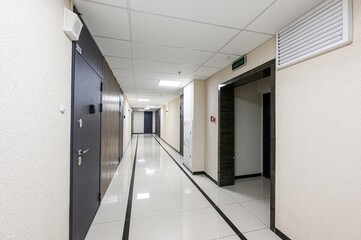 interior shot of a long corridor with tiled flooring, doors on either side, and a ceiling with...