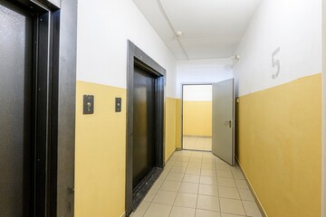 Hallway with elevators and a door. The walls are painted yellow and white with tiled floors and a number '5' painted on the wall
