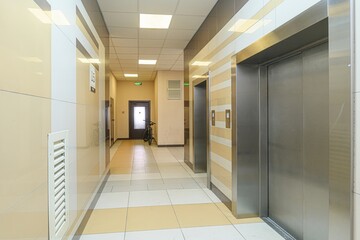 bright hallway shows elevators to the right and a dark door to the left with a bicycle parked...