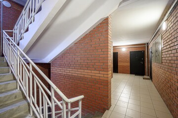 Interior shot of a building hallway with stairs. Brick walls, tiled floor, and a white staircase...
