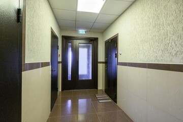well-lit hallway with dark doors and tiled floor.  An exit sign hangs above the central door