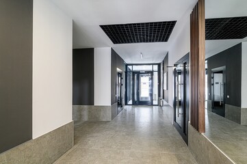 modern interior hallway with tiled floor, dark accent walls, grid ceiling, and glass doors