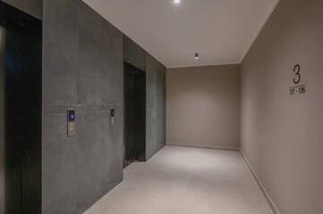 Modern lobby with gray elevators and tile walls. A beige wall with 