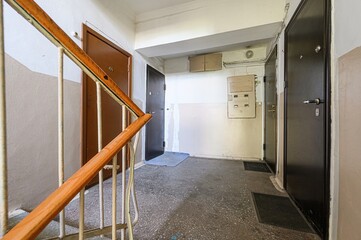 worn hallway with doors, stairs, a wooden railing, and a concrete floor. The walls are peeling paint, with mailboxes