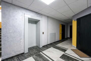 modern hallway with an elevator, apartment doors, and tile flooring. Walls are a textured grey,...