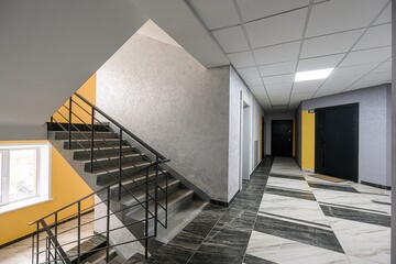 Modern building interior with stairs, a hallway featuring patterned tile, and doors along a painted...