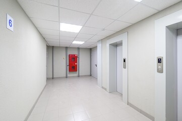 bright hallway featuring elevators, a fire hose cabinet, tiled floor and a number '6' sign on the...