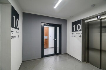modern hallway with neutral colors. There are signs with the number 10, an elevator, and a door