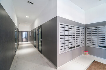Modern apartment hallway with mailboxes and office doors. The space is clean with gray and white...