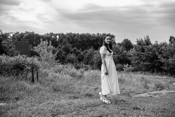 Portrait of a young beautiful dark-haired girl in a dress in the forest. Vintage black and white...