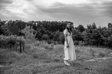 Portrait of a young beautiful dark-haired girl in a dress in the forest. Vintage black and white...