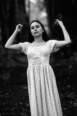 Portrait of a young beautiful dark-haired girl in a dress in the forest. Vintage black and white...
