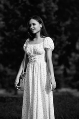 Portrait of a young beautiful dark-haired girl in a dress in the forest. Vintage black and white...
