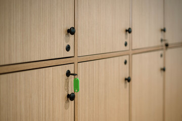 Close-up of light wood lockers with black knobs. A key with a green tag is in one lock, focusing on...