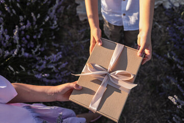 Close-up of two children exchanging a kraft gift box with a ribbon and a lavender bouquet in a...