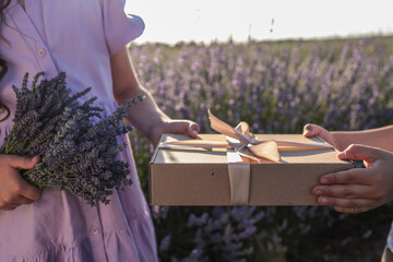 Close-up of two children exchanging a kraft gift box with a ribbon and a lavender bouquet in a...