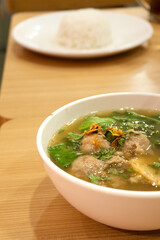 Delicious and savory meatball soup in a white bowl with a sprinkling of celery and fried onions.