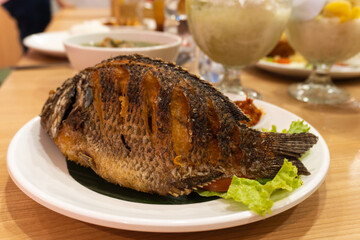 Delicious fried fish with rice, cucumber, lettuce, tomato with Indonesian spicy chili sauce.