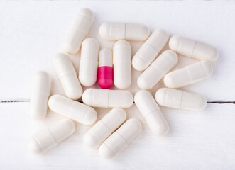 white capsules and one red one with medicine on a white background, close-up