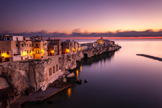 Coastal town of Vieste, Italy, captured during twilight using long exposure technique, highlighting warm street lights, dramatic cliffs, and a serene Adriatic Sea.