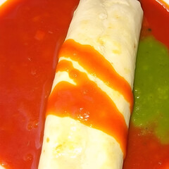 Three colored wet burrito served in red and green sauce, looks and tastes appealing.