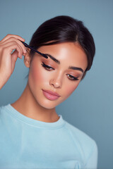 makeup artist fixing brows with pastel background