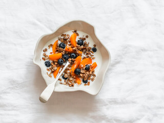 Delicious healthy breakfast - greek yogurt with granola, apricots and blueberries in a ceramic bowl