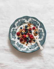 Greek yogurt with granola, raspberries and blueberries in a vintage plate on a white background
