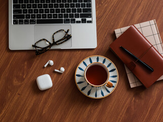 Laptop, cup of tea, notebook, glasses, headphones on a wooden table, top view
